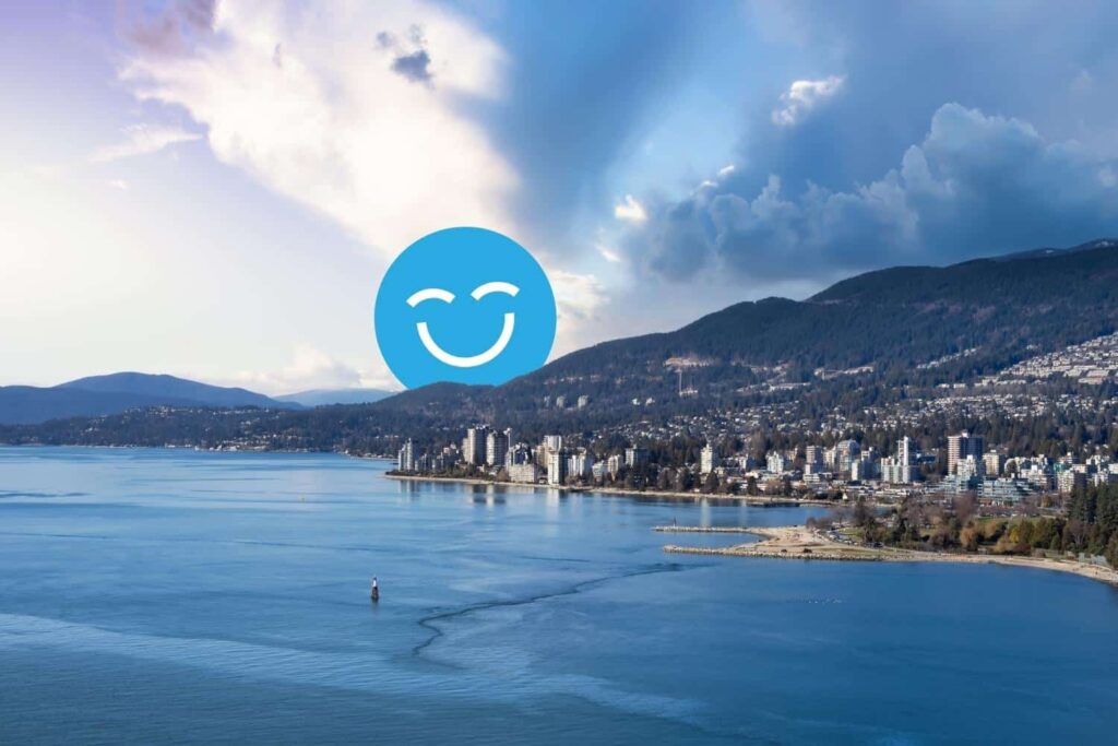 Coastal city skyline at dusk with mountains in the background and a large smiling blue face icon in the sky.