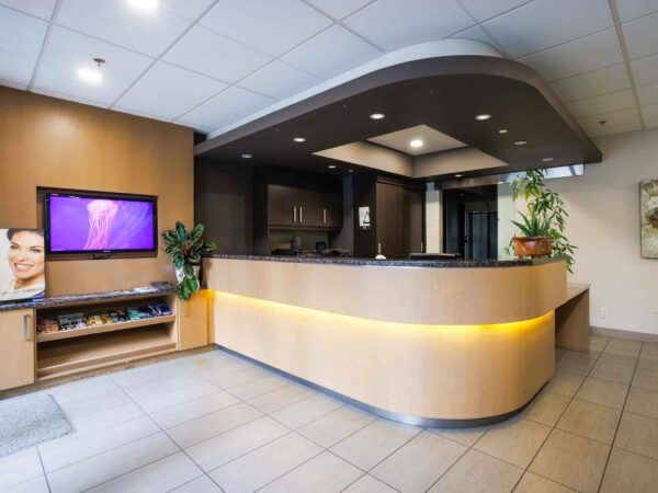 A modern reception area featuring a curved desk, a wall-mounted screen displaying colorful content, and plants. The space has neutral tones and a welcoming ambiance, designed for a professional setting.