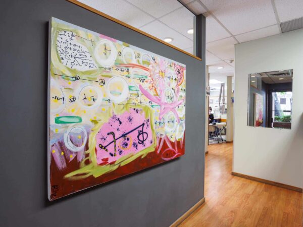 A colorful abstract painting featuring musical notes and vibrant shapes hangs on a wall in a bright interior space, with wooden flooring and contemporary decor visible in the background.