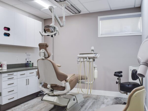 A modern dental office featuring a comfortable dental chair, an examination light, and various dental instruments. The room has light-colored walls and a window providing natural light, creating a clean and welcoming environment.