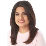 A woman with long, dark hair and a warm smile poses for a portrait against a white background. She is wearing a light pink top and appears friendly and approachable.