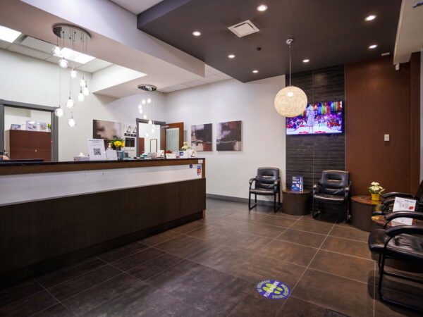 A modern reception area featuring a sleek check-in desk, several black chairs, and a colorful wall-mounted screen. Bright lighting and a minimalist design create a welcoming atmosphere.