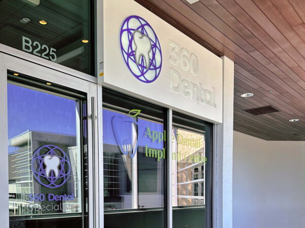A modern dental office entrance features the sign "360 Dental" with a tooth logo. The glass doors display additional text about dental implants, and the overall design emphasizes a welcoming and professional atmosphere.