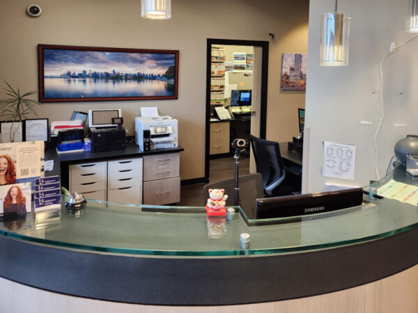 A modern reception area featuring a curved front desk, promotional materials, a monitor, and a comfortable chair. The background includes a scenic artwork and an open door leading to another office space. Soft lighting enhances the welcoming atmosphere.